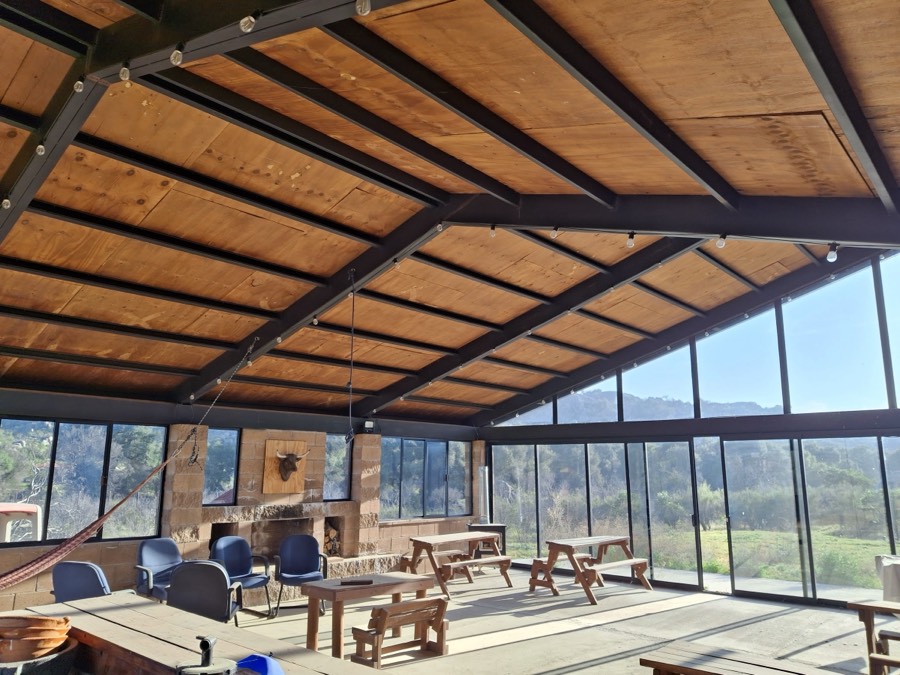 El interior de la nave: techo de madera a dos aguas, ventanales de piso a techo y mesas largas de madera.